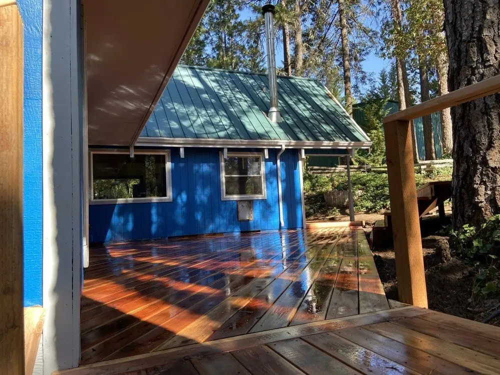 Blue board-and-batten cabin with a green metal roof and a freshly built wood deck, by Next Gen Contracting in Southern Oregon