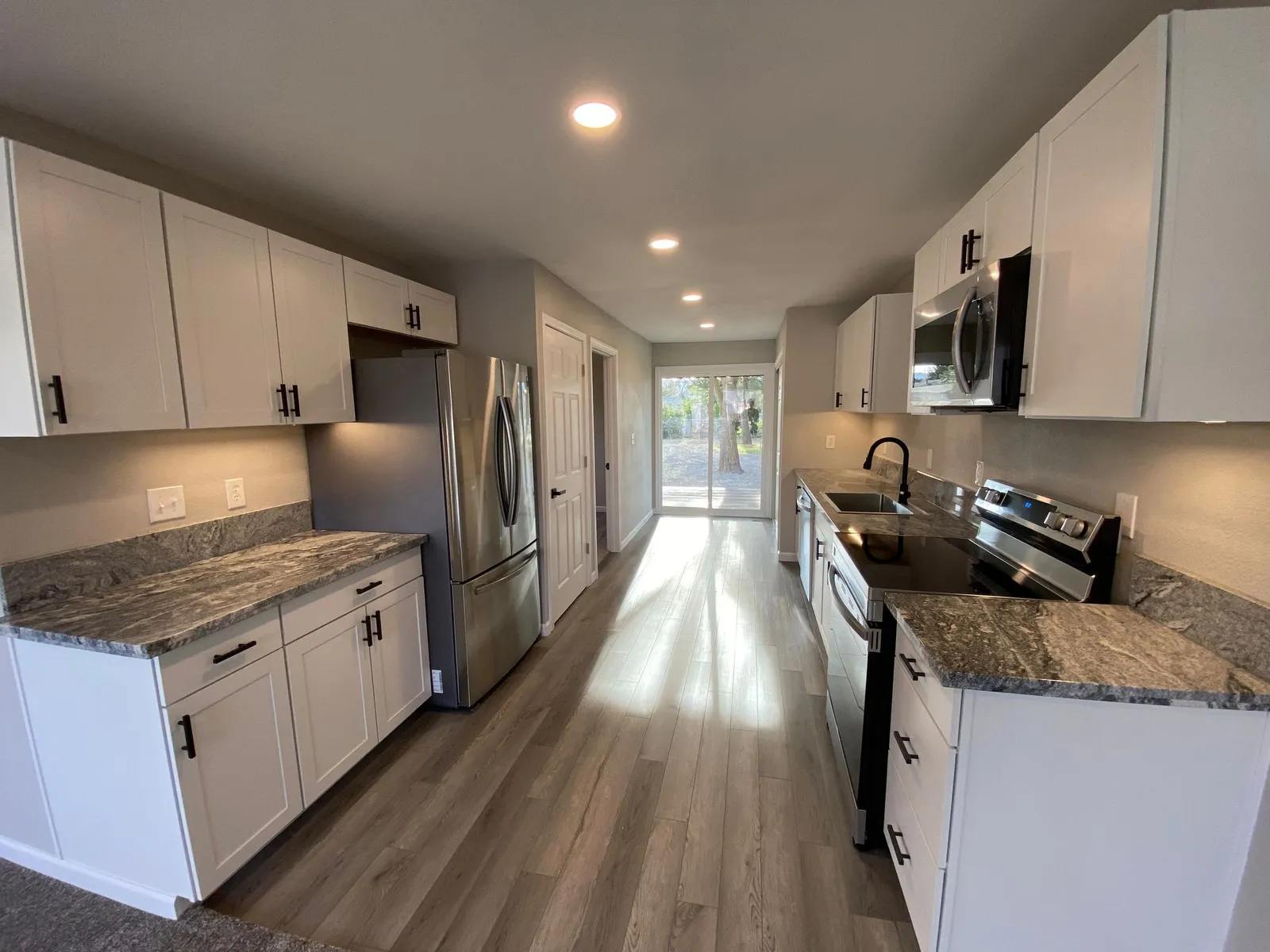 Remodeled kitchen with white shaker cabinets, stone countertops, and stainless appliances by Next Gen Contracting in Medford, Oregon